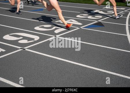 Outdoor track and fiield running race on a gray track with numbered lanes and a finish line with copy space. Two runners cross the line. Stock Photo