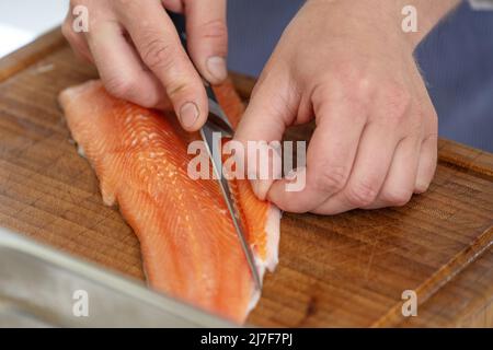 Hands of a cook remove the belly flap with bones of a fresh raw char fish with a filleting knife on a cutting board, selected focus, narrow depth of f Stock Photo