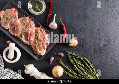 top view of the black background with a tray of prepared farm pork steaks for baking with spices and rosemary. delicious food Stock Photo