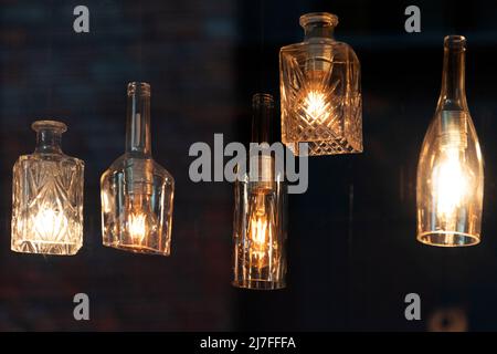 Lanterns made of glass bottles and Edison lamp bulbs. DIY lamps made from recycled old bottles hanging in cafe window Stock Photo