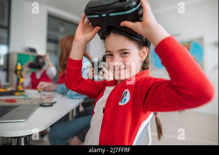 Happy schoolgirl wearing virtual reality goggles at school in computer science class Stock Photo