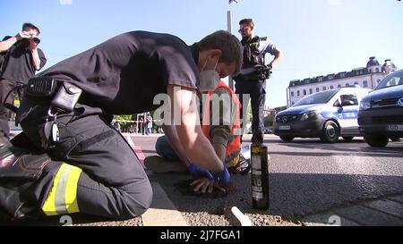 Leipzig, Germany. 09th May, 2022. Environmental activists of the group 'Last Generation' stuck themselves on the roadway and a policeman tried to remove the glue. Police task forces cordoned off the area and removed the protesters. Traffic was backed up over a wide area. Credit: Tobias Junghannß/TNN/dpa/Alamy Live News Stock Photo