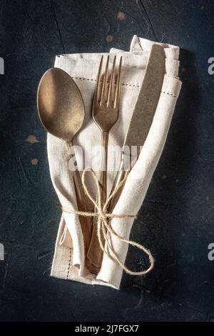 Cutlery. A spoon, a fork, and a knife in a rustic napkin on a black background. Modern silverware on a dark table, shot from above Stock Photo