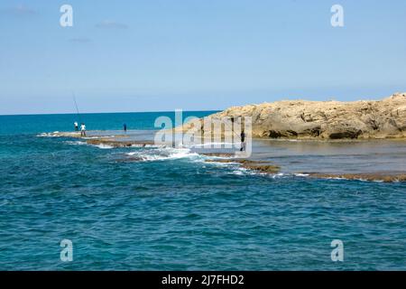 Rock Formation and fishermen at Dor-Habonim beach, Israel Stock Photo