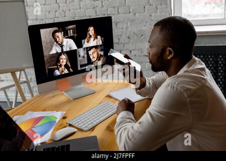 African american male freelancer waving hello to coworkers on video meeting, using laptop. Stylish friendly businessman having a video meeting Stock Photo