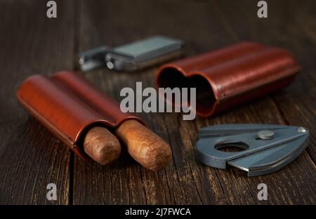 View of a leather case with two Cuban cigars, a lighter and a cutter on a wooden table top. Stock Photo