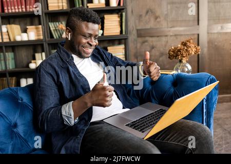 Joyful african american manager wear headphones looking laptop provide support to client distantly, hold online conference. Student study distantly at Stock Photo