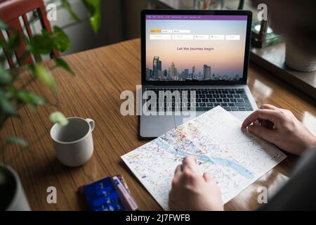 Man searching for flights on laptop and looking at map Stock Photo
