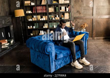 Smiling young african american student or business man professional making business call on the yellow laptop at home enjoying corporate conversation Stock Photo