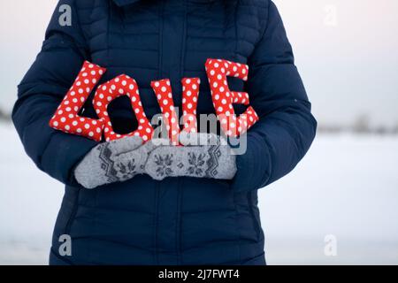 Girl in blue down jacket and gloves holding a sign 'Love' Stock Photo