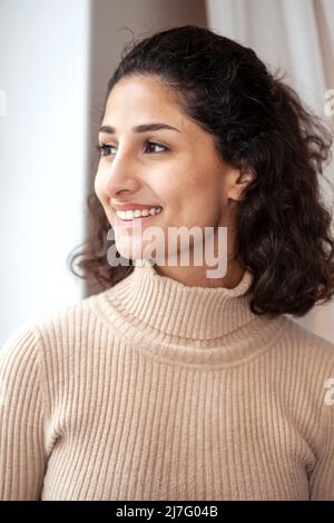 Smiling young woman looking through window Stock Photo