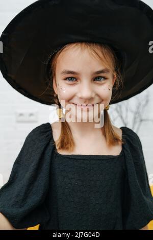 Happy smiling girl in a witches hat with glitter on her cheeks. looking off camera, portrait. Stock Photo