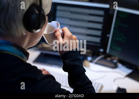 Male programmer working on computer and drinking from mug Stock Photo