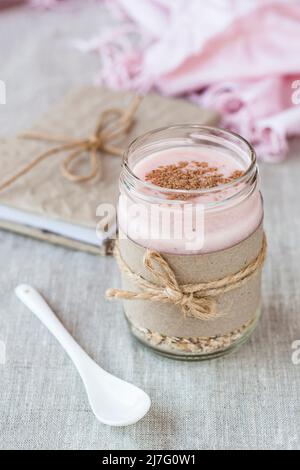 Oatmeal, flavored with yogurt, sprinkled with cinnamon in a glass jar. Next is a craft notebook and a pink napkin. Stock Photo