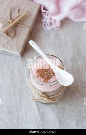 Oatmeal, flavored with yogurt, sprinkled with cinnamon in a glass jar. Next is a craft notebook and a pink napkin. Stock Photo