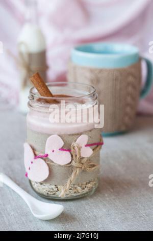 Oatmeal, flavored with yogurt, sprinkled with cinnamon in a glass jar. Next is a cup of coffee and a bottle of milk. Next is a craft notebook and a pi Stock Photo