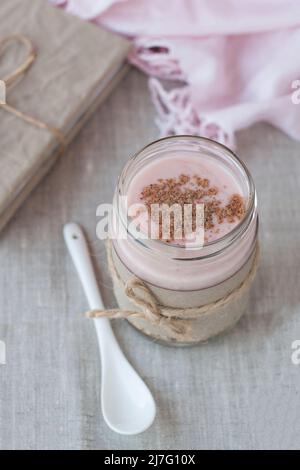 Oatmeal, flavored with yogurt, sprinkled with cinnamon in a glass jar. Next is a craft notebook and a pink napkin. Stock Photo