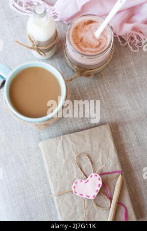 Oatmeal, flavored with yogurt, sprinkled with cinnamon in a glass jar. Next is a cup of coffee and a bottle of milk. Next is a craft notebook and a pi Stock Photo