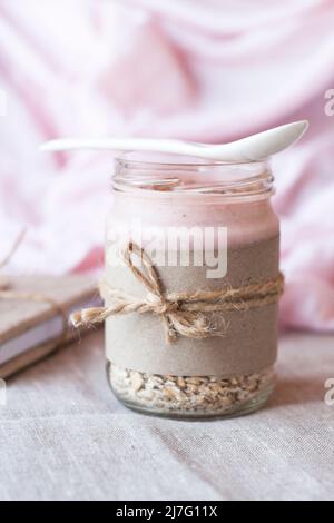 Oatmeal, flavored with yogurt, sprinkled with cinnamon in a glass jar. Next is a craft notebook and a pink napkin. Stock Photo