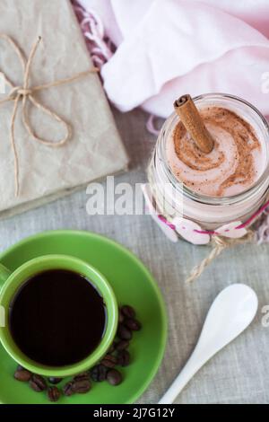 Oatmeal, flavored with yogurt, sprinkled with cinnamon in a glass jar. Next is a cup of coffee. Next is a craft notebook and a pink napkin. Stock Photo