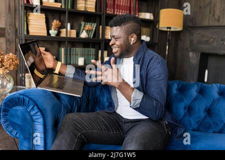 Happy young male black freelancer talking on conference video call to colleagues online. Afro American student talking to teacher and other students Stock Photo