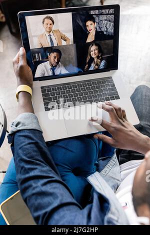Back view of african american male freelancer showing thumbs up to coworker on video meeting, using laptop. Stylish friendly businessman come to Stock Photo