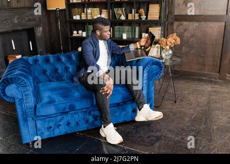 Satisfied African American male relaxing at sofa coach with laptop on legs, joyful man businessman freelancer student dreaming, resting after work Stock Photo