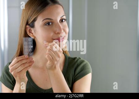 Beautiful young woman applying acne treatment anti-pickel patch on a pimple in bathroom at home Stock Photo