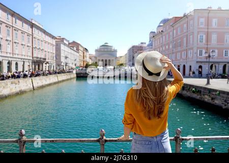 Travel in Trieste, Italy. Back view of pretty girl holding hat looking at Sant Antonio Taumaturgo church on Grand Canal in Trieste, Italy. Beautiful y Stock Photo