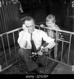 Father in the 1940s. Actor Åke Söderblom, 1910-1965 tries his best at amusing his son from outside the playpen, but it is first when he changes places with his son and puts himself inside the playpen his son gets happy. Sweden 1949 AN94-5 Stock Photo