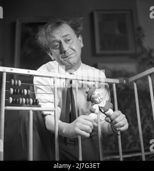 Father in the 1940s. Actor Åke Söderblom, 1910-1965 tries his best at amusing his son from outside the playpen playing with a a doll. Judging by the look on his face he has no success in cheering up his son.  Sweden 1949 AN93-3 Stock Photo