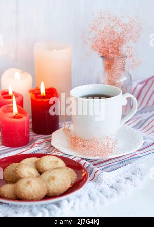 A hot cup of black tea with homemade cookies on a striped tablecloth, wax candles, a glass vase with decorative herbs on a white background. Stock Photo