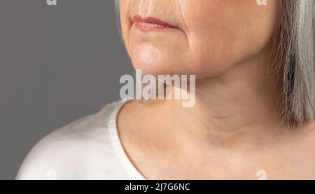 Mature skin care. Cropped view of senior woman's face with wrinkles around lips and on neck, grey studio background Stock Photo