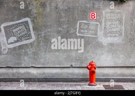 Fire hydrant in front of a gray wall with global warming tags. Brussels. Stock Photo