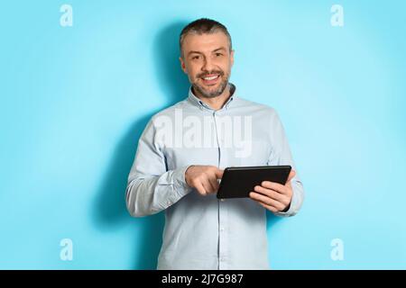 Middle Aged Man Using Tablet Browsing Internet On Blue Background Stock Photo