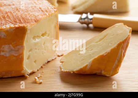 Piece of French Le Chandor cheese with an orange crust close up on a cutting board Stock Photo