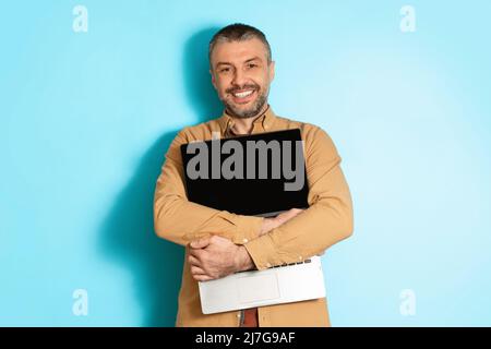 Joyful Middle Aged Man Hugging New Laptop On Blue Background Stock Photo