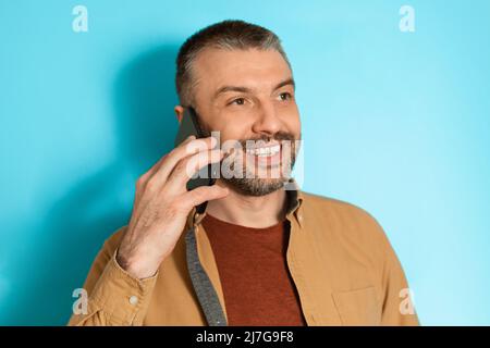 Happy Man Talking On Cellphone Looking Aside Over Blue Background Stock Photo