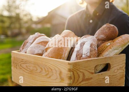 A baker woman holds fresh bread in her hand against the background of bakers  working in a bakery Stock Photo - Alamy