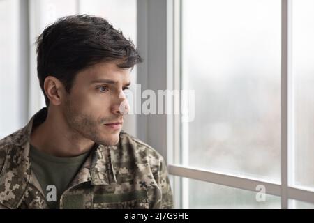 Unhappy military man looking through window at home Stock Photo