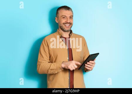 Middle Aged Business Man Using Digital Tablet Over Blue Background Stock Photo
