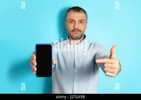 Serious Male Showing Cellphone Screen Pointing Finger Over Blue Background Stock Photo