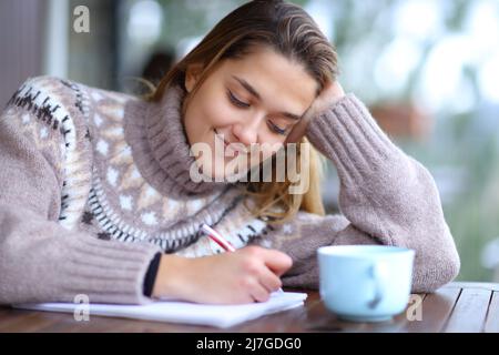 Happy woman taking notes in a bar terrace in winter Stock Photo