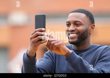 Happy man with black skin taking selfie or photo with smart phone standing in the street Stock Photo