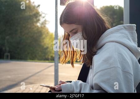 A young teenage woman is waiting for a bus at a bus stop early in the morning. Stock Photo