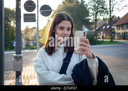 A young teenage woman is waiting for a bus at a bus stop early in the morning. Stock Photo
