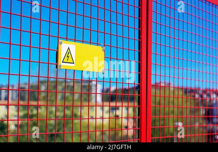 High voltage warning sign hanging from the red grille somewhere in Poland Stock Photo