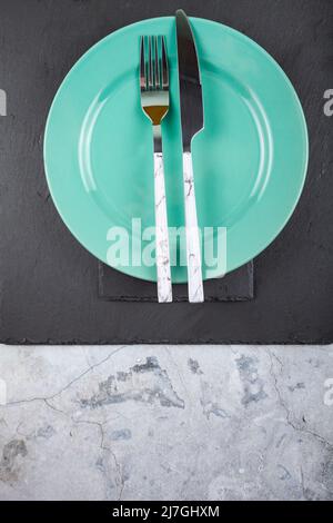 Flat lay composition with green plate, fork and knife on black slate board. Marble background. Stock Photo