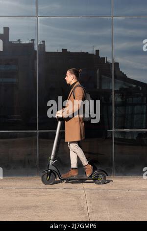 Vertical view of young elegant bussinesman riding an electric scooter around the financial district of the city center Stock Photo