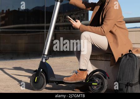 Electric scooter rent with mobile phone. Man using smartphone rental app in city street. Modern transportation and commute technology. Stock Photo